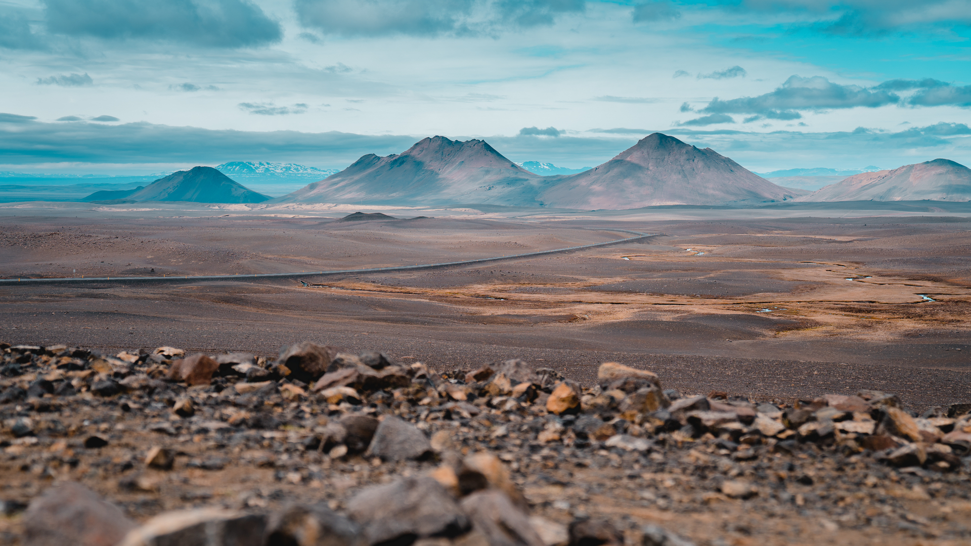Paisaje volcánico cerca de Egilsstaðir, Islandia, con montañas y carretera entre terrenos áridos bajo cielo azul.