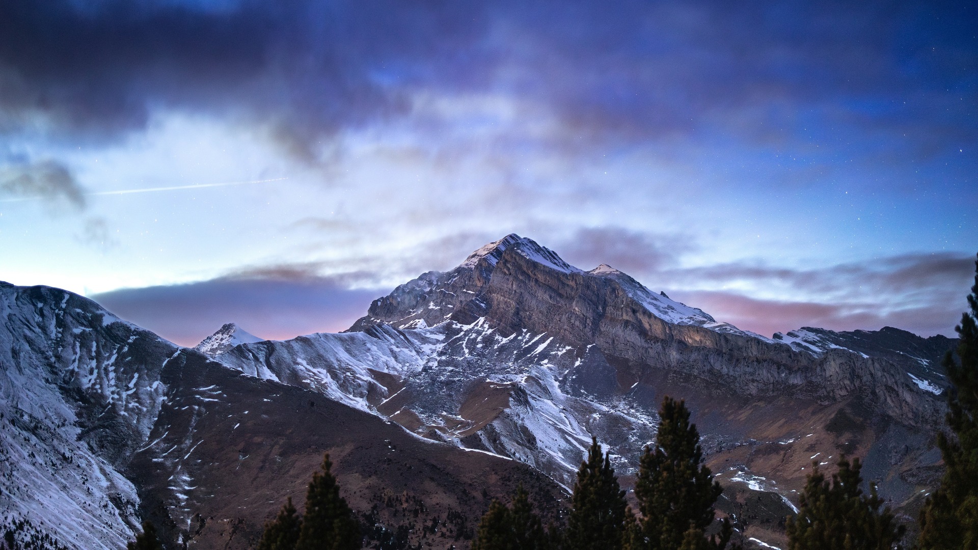 Paisaje nocturno de montaña nevada bajo un cielo estrellado y nublado en Aínsa.