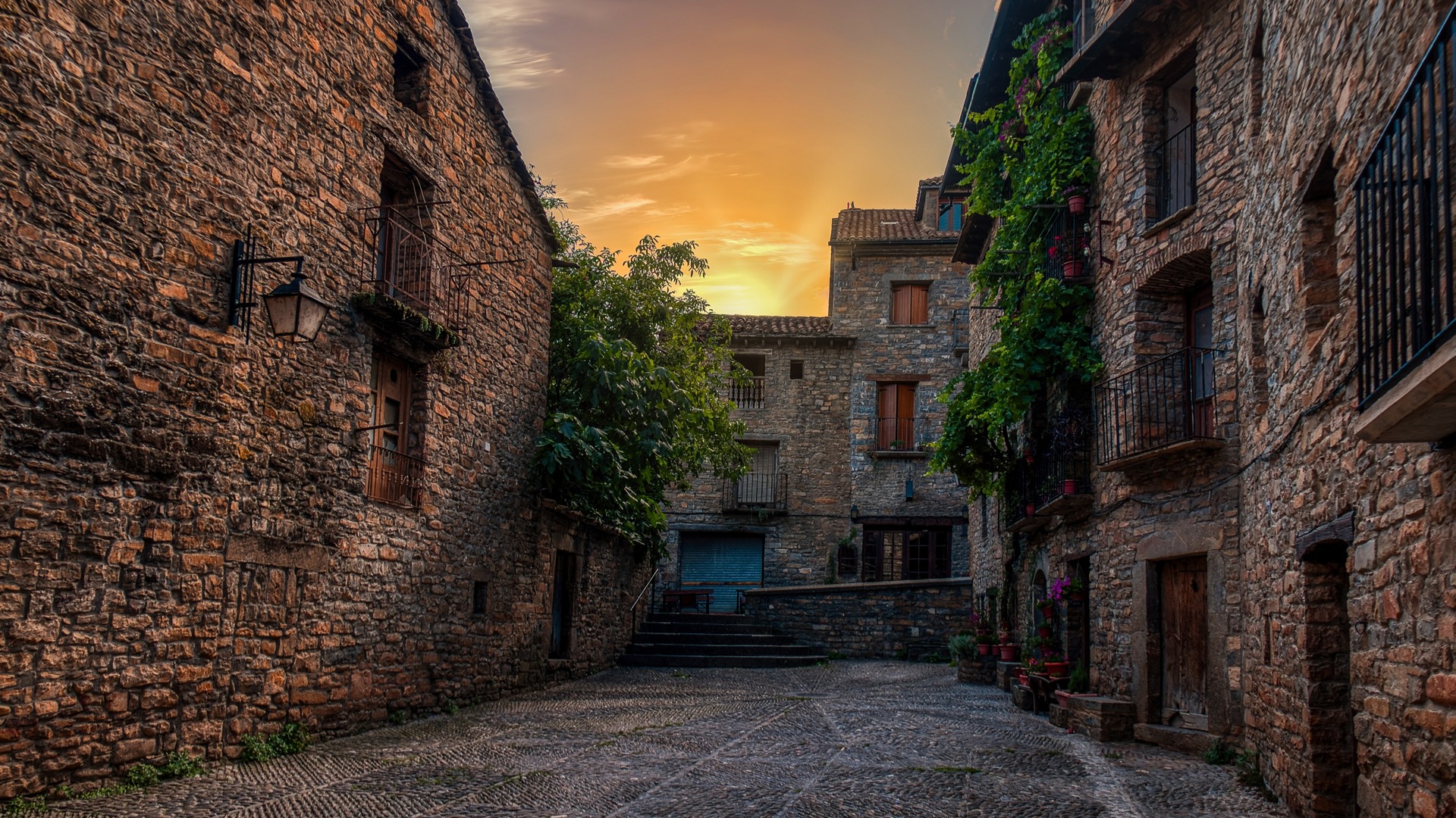 Calle empedrada rodeada de casas de piedra con balcones en la villa medieval de Aínsa.