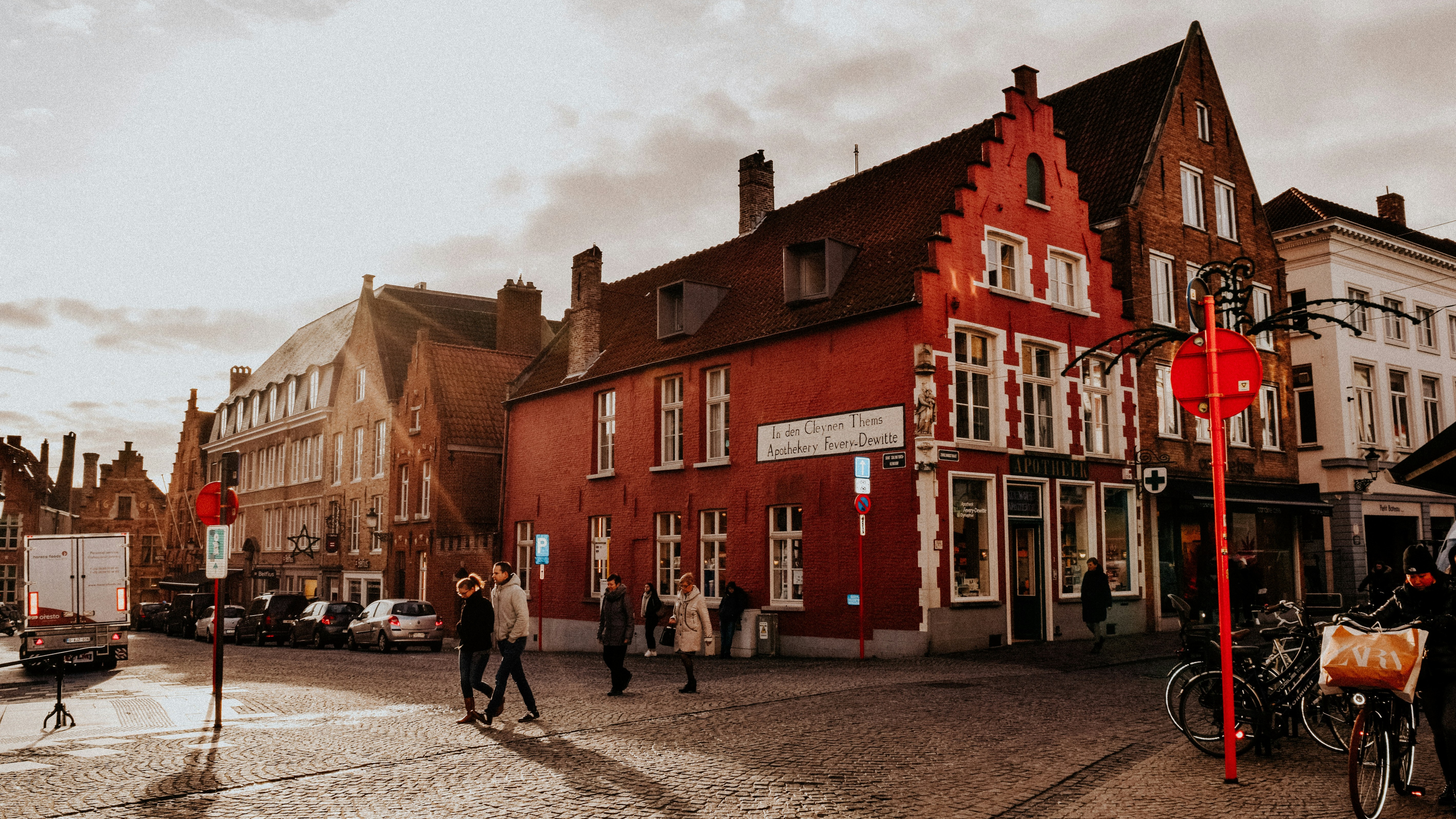Turistas caminando frente a una antigua botica roja en el centro de Brujas.