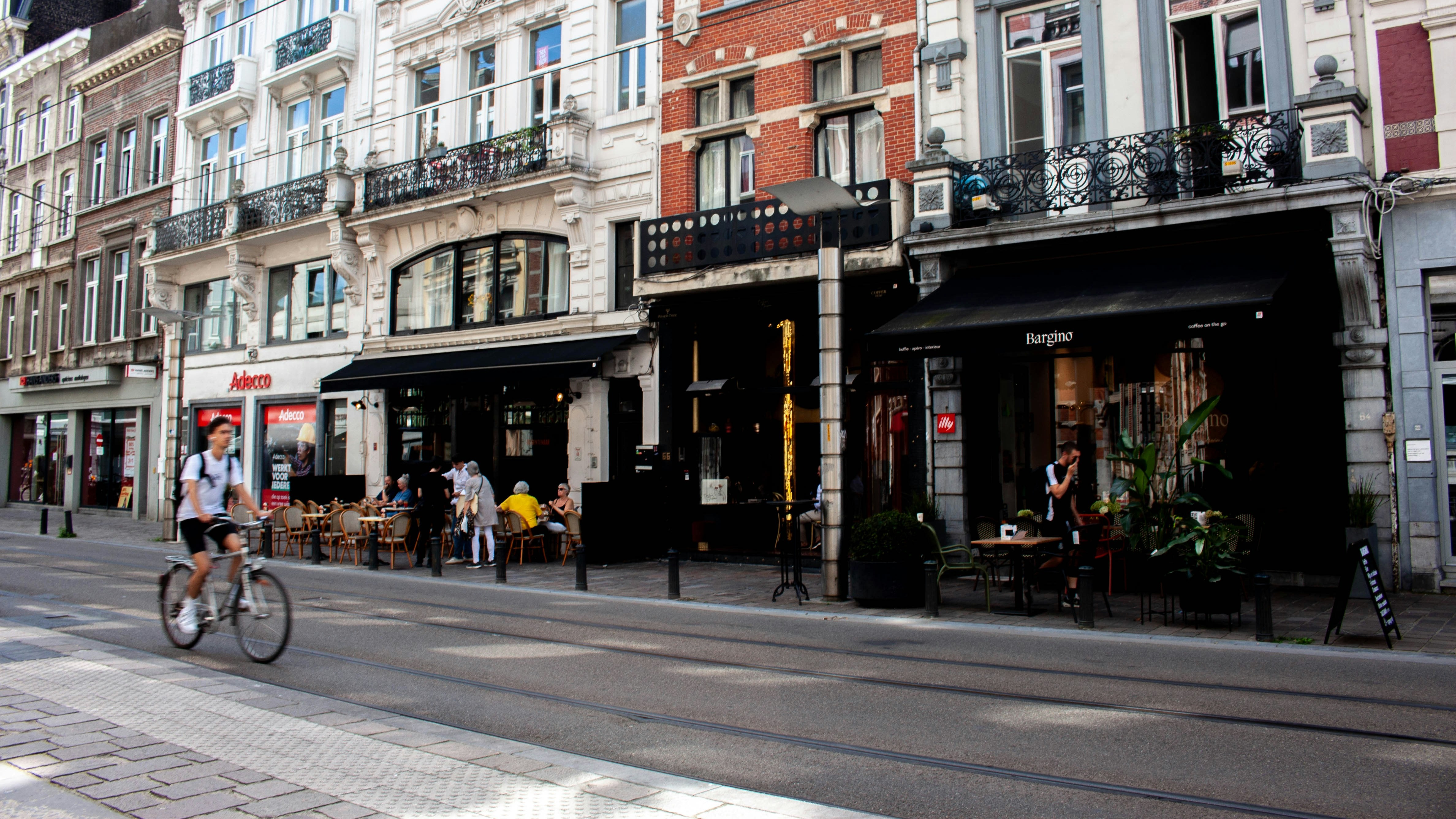Ciclista pasando frente a cafeterías con terrazas en una calle de Gante.