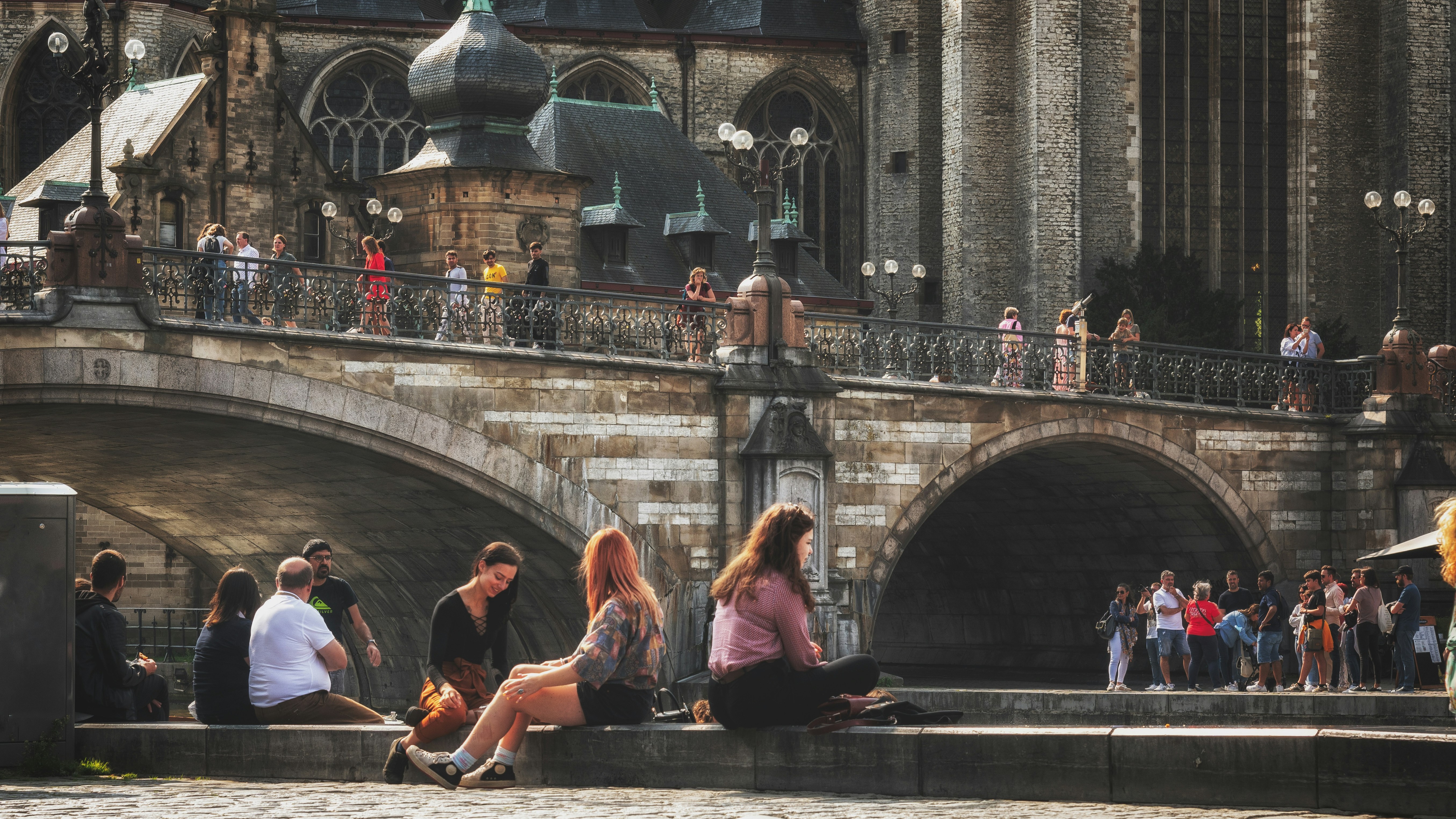 Jóvenes sentados junto al canal bajo el Puente de San Miguel en Gante.