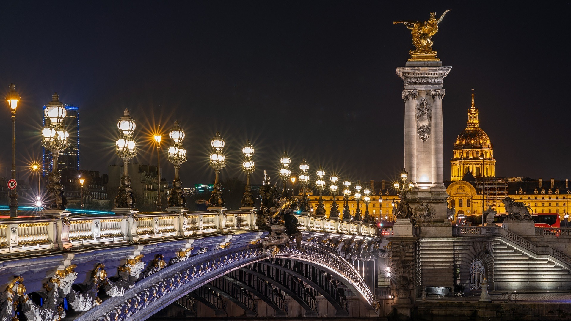 Puente Alejandro III iluminado de noche con Los Inválidos al fondo en París.