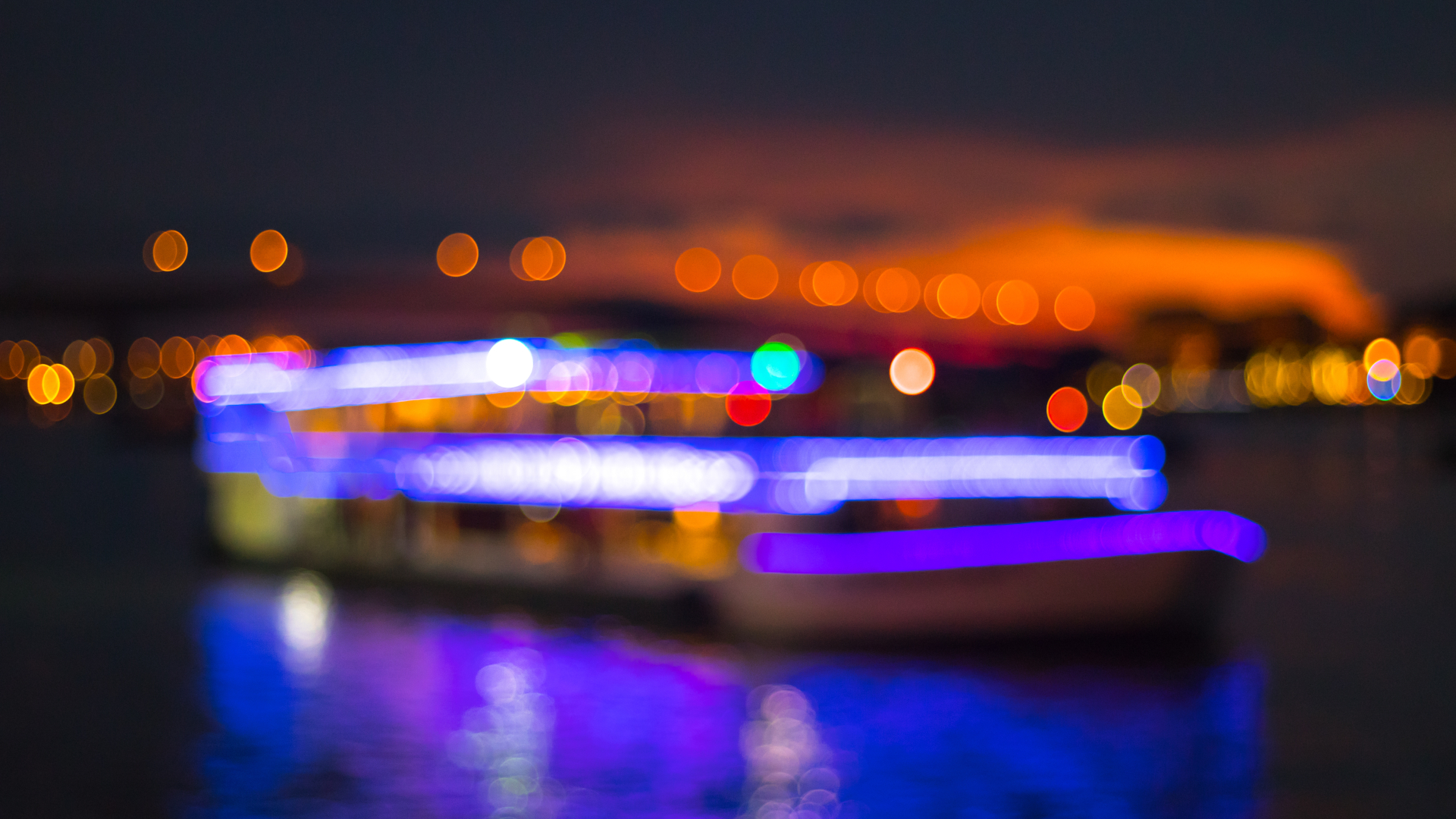 Barco iluminado con luces de colores navegando de noche.