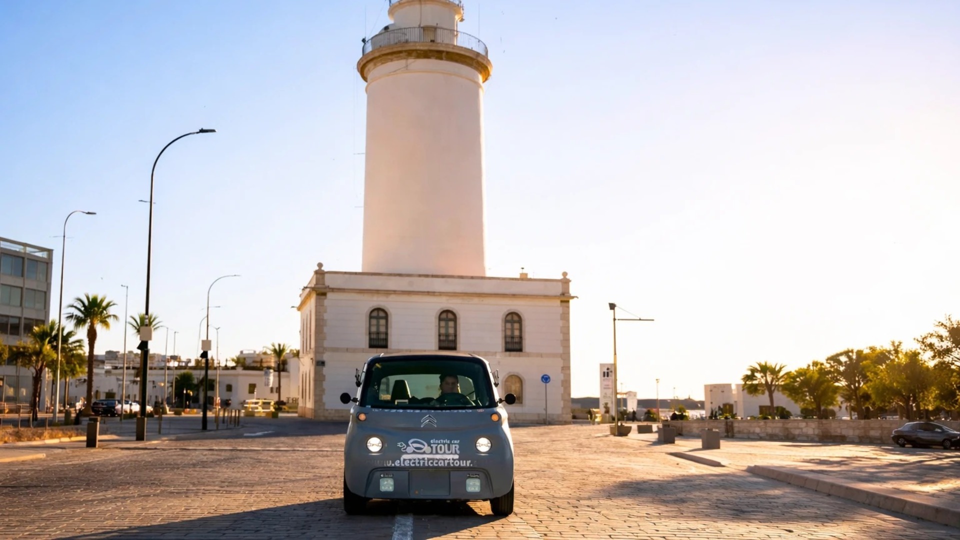 Coche eléctrico de tour frente al faro La Farola en el puerto de Málaga.