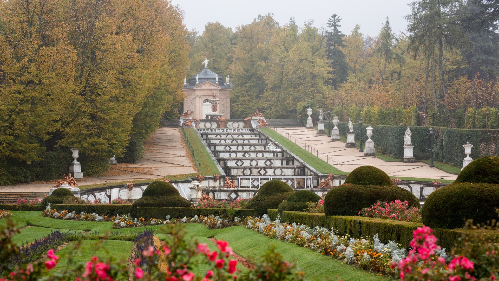 La Cascada Nueva de La Granja rodeada de árboles otoñales y estatuas blancas.