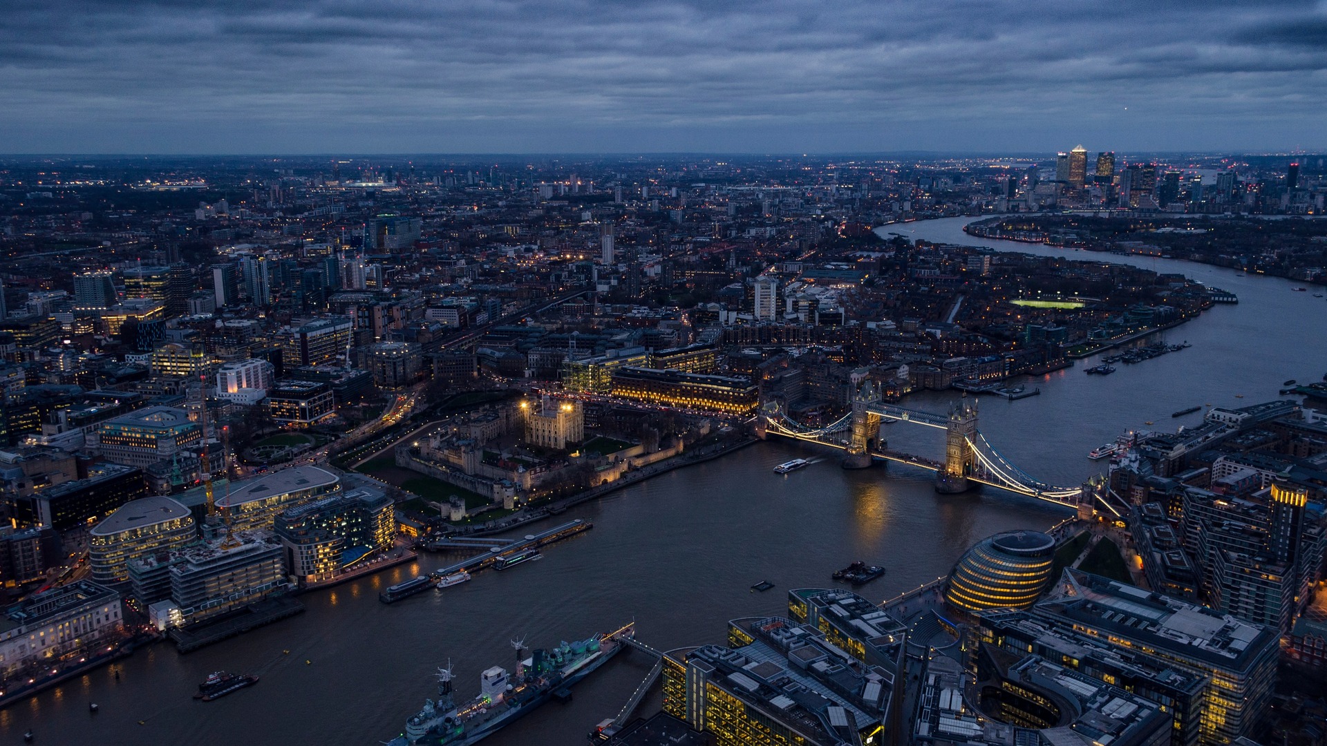 Vista aérea panorámica del río Támesis en Londres con el Puente de la Torre iluminado y la Torre de Londres al anochecer.