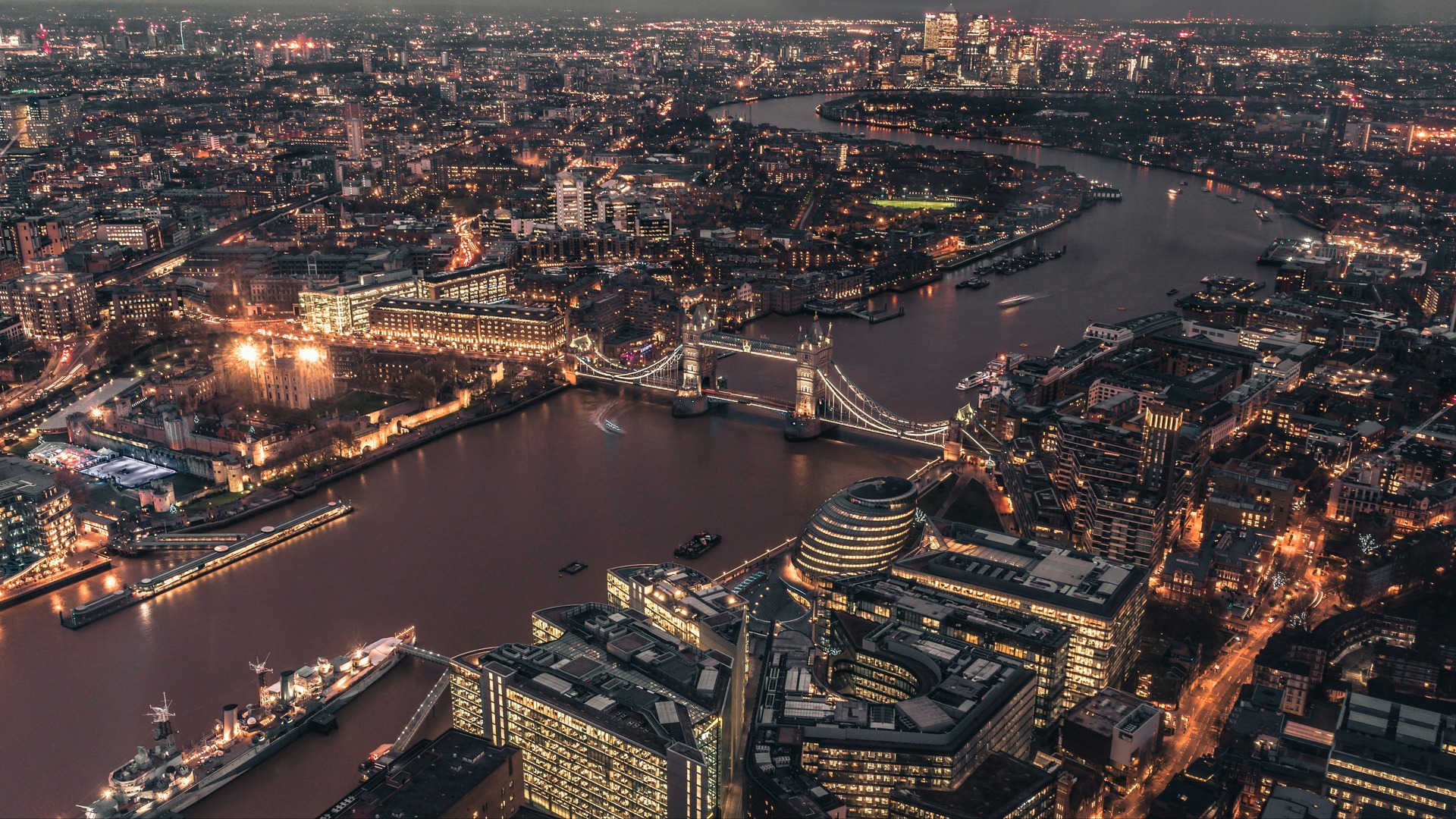 Vista aérea nocturna de Londres con el Tower Bridge iluminado cruzando el Támesis y la Torre de Londres en primer plano.