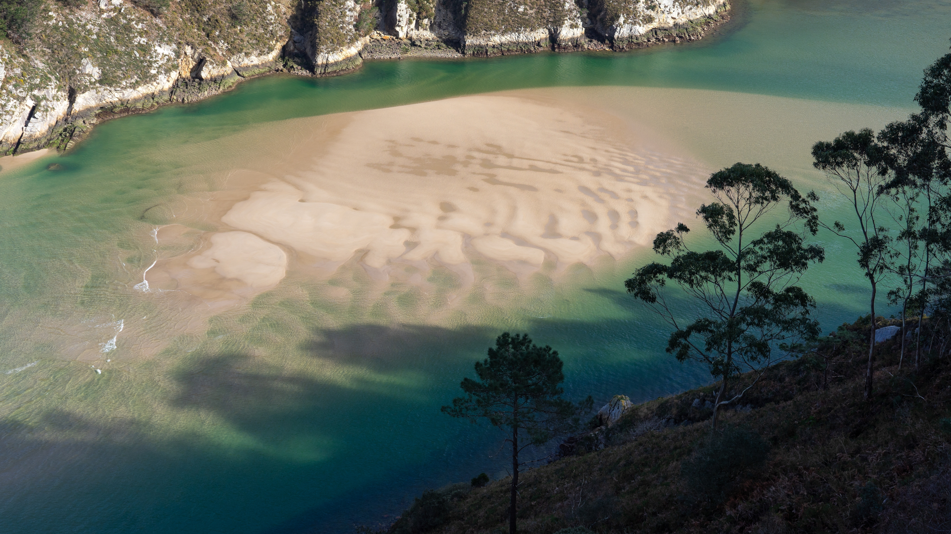 Banco de arena y aguas turquesas en la costa de Pechón, Cantabria.