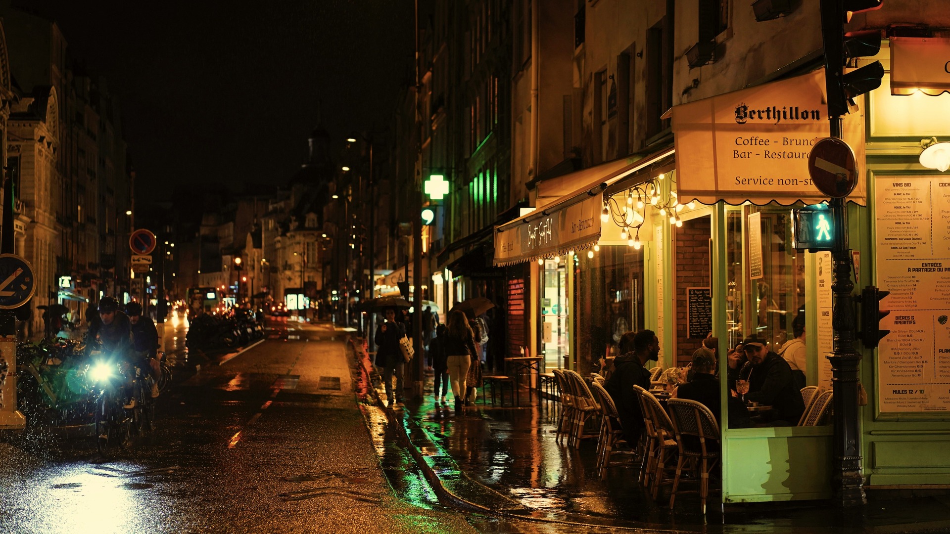 Gente cenando en la terraza iluminada del café Berthillon en una noche de París.