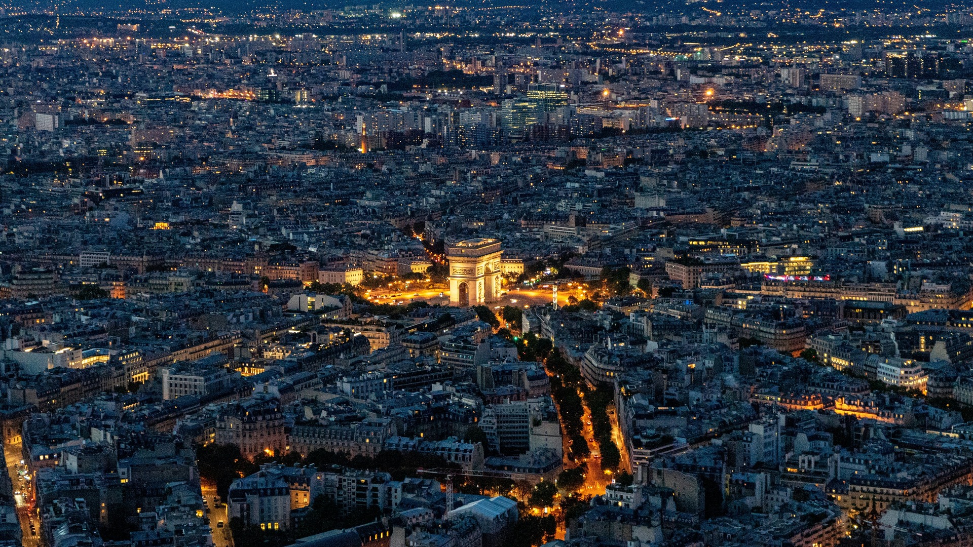 Vista aérea nocturna del Arco del Triunfo iluminado y el horizonte de París.