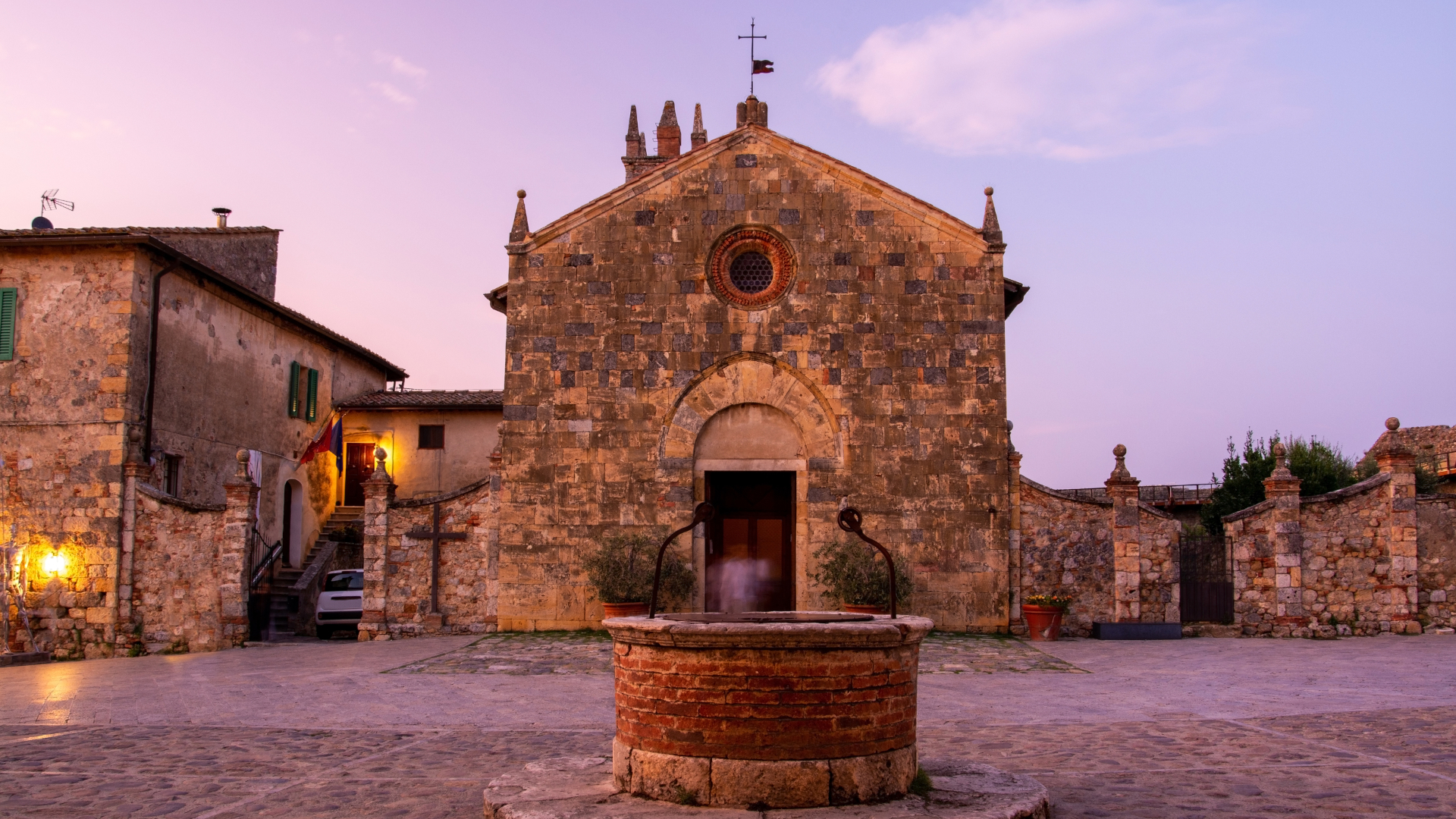 Plaza con iglesia medieval y fuente al atardecer en la Toscana, Italia