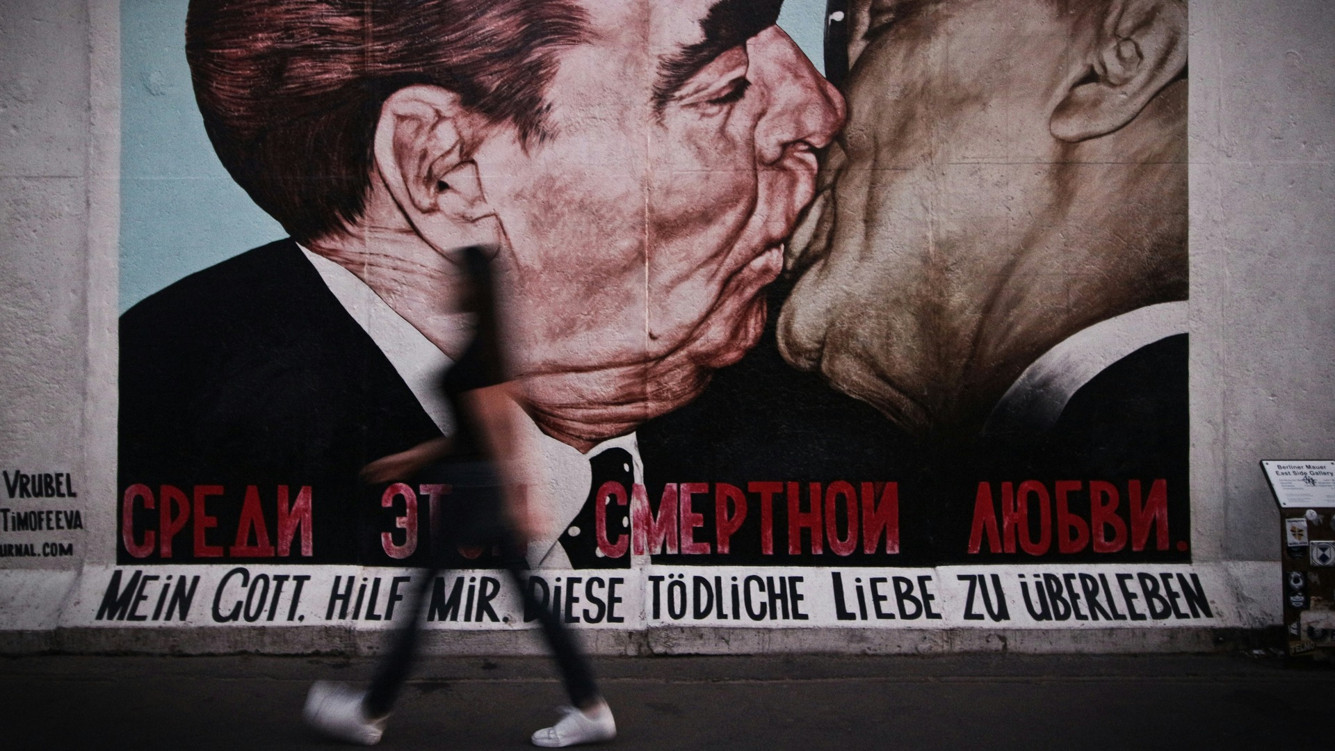 Mural del beso en el Muro de Berlín con silueta de persona caminando delante.