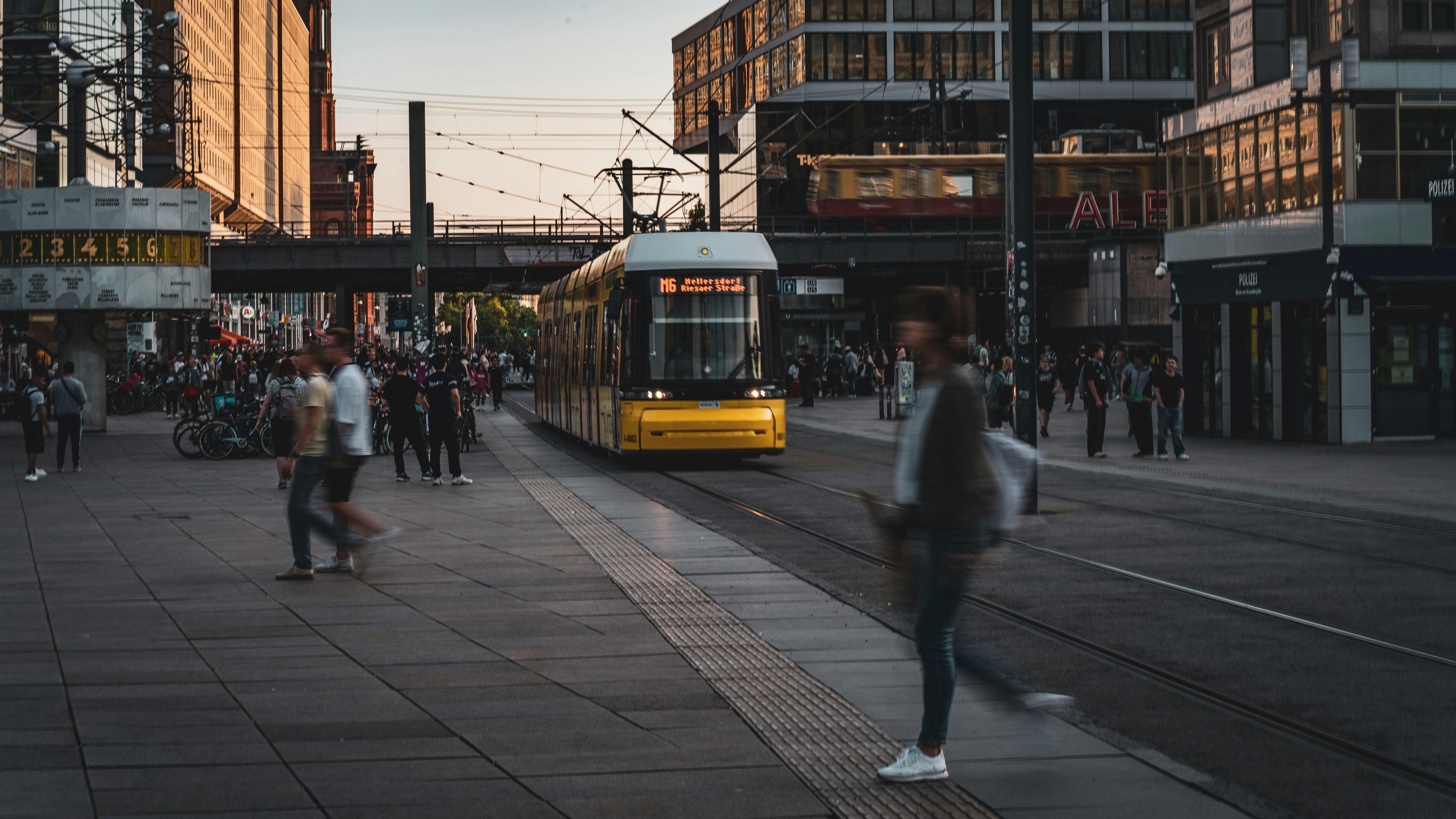 Tranvía amarillo circulando por Alexanderplatz en Berlín con peatones en movimiento.