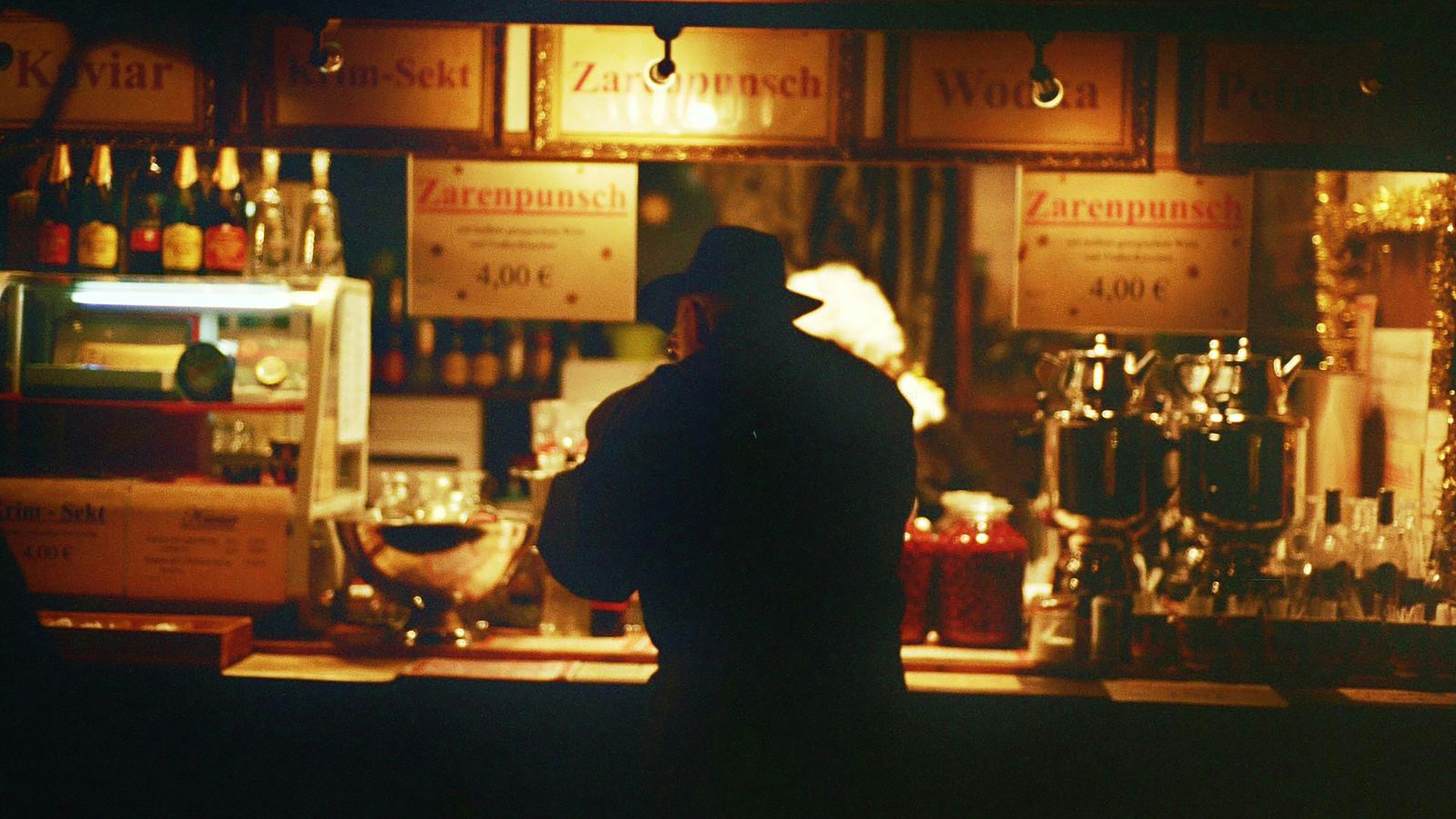 Silueta de hombre con sombrero frente a un puesto de bebidas en Berlín.