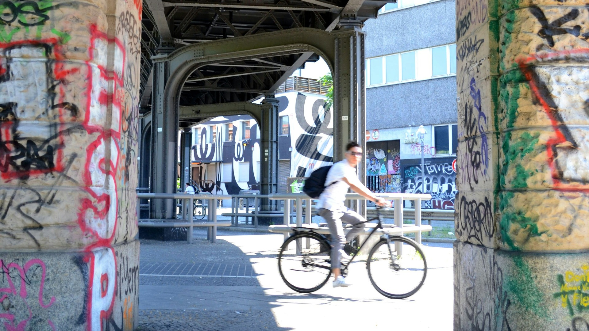 Ciclista pasando bajo una estructura de hierro con grafiti en Berlín.