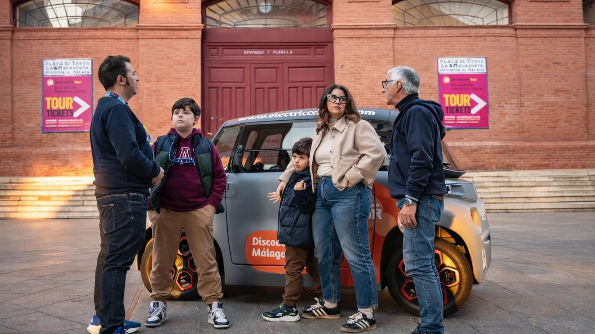 Familia junto a un coche eléctrico frente a la Plaza de Toros de Málaga.