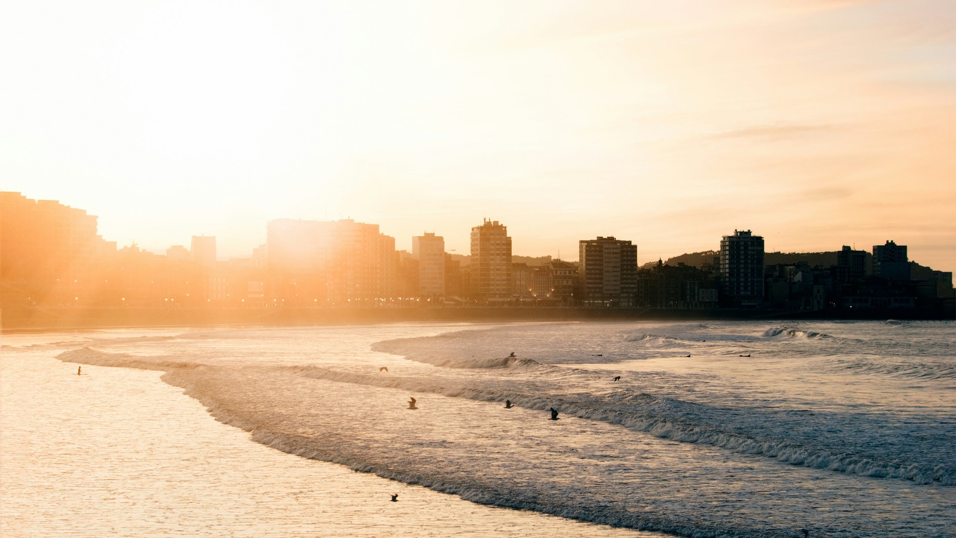 Atardecer dorado sobre las olas de la Playa de San Lorenzo y el skyline de Gijón.