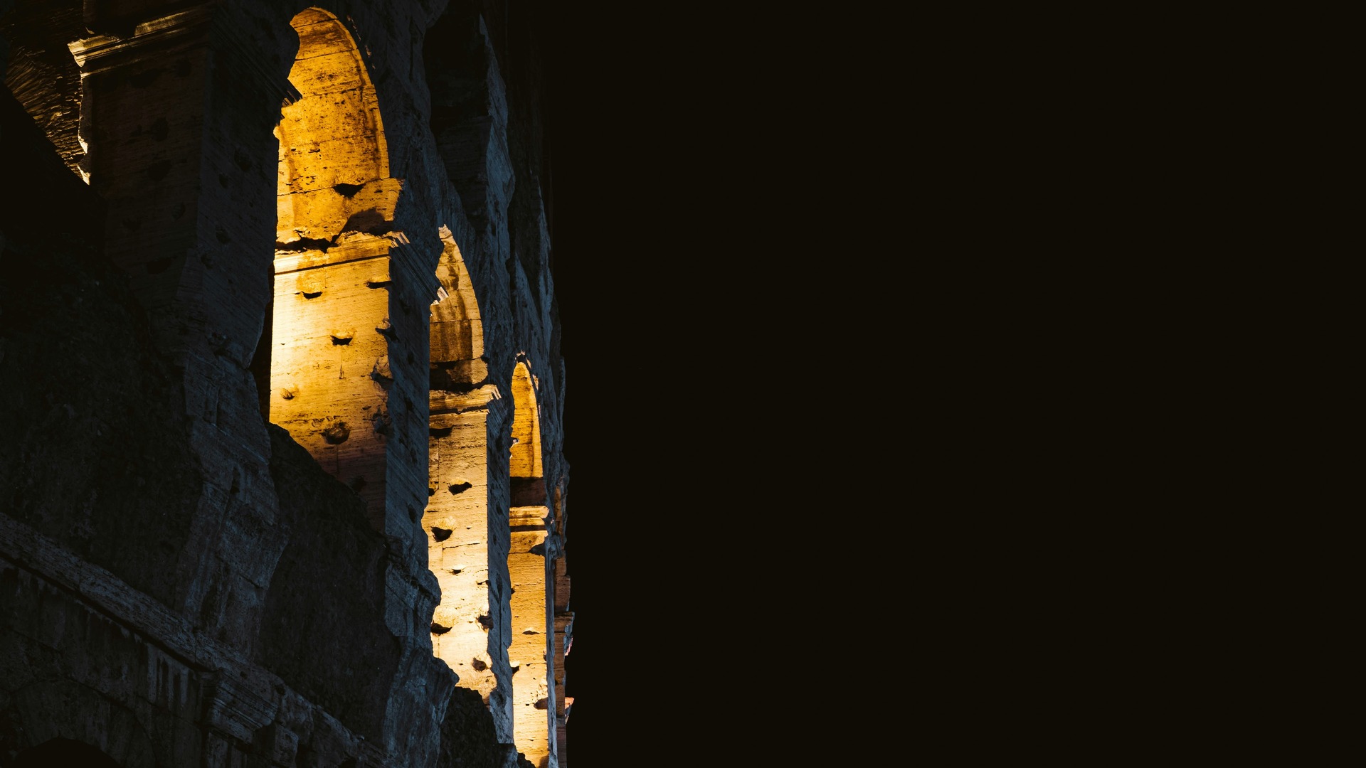 Arcos iluminados del Coliseo Romano resaltando sobre un fondo negro nocturno.