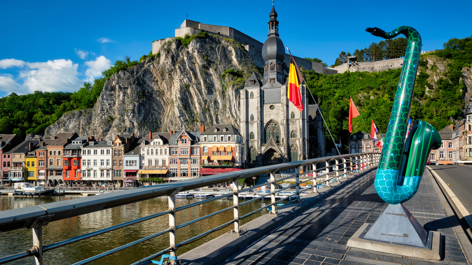 Escultura de saxofón en puente de Dinant con la Colegiata y ciudadela al fondo