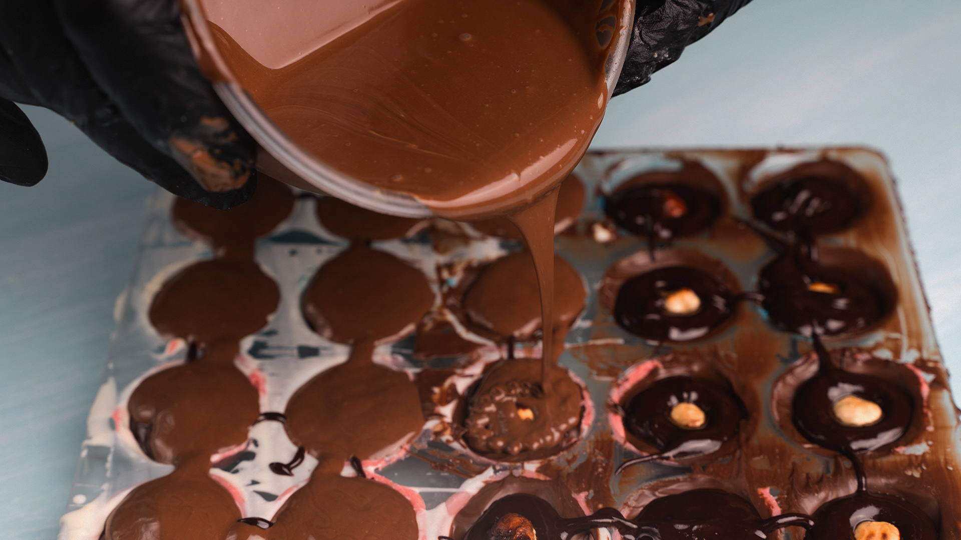 Vertido de chocolate derretido sobre molde con avellanas en obrador artesanal