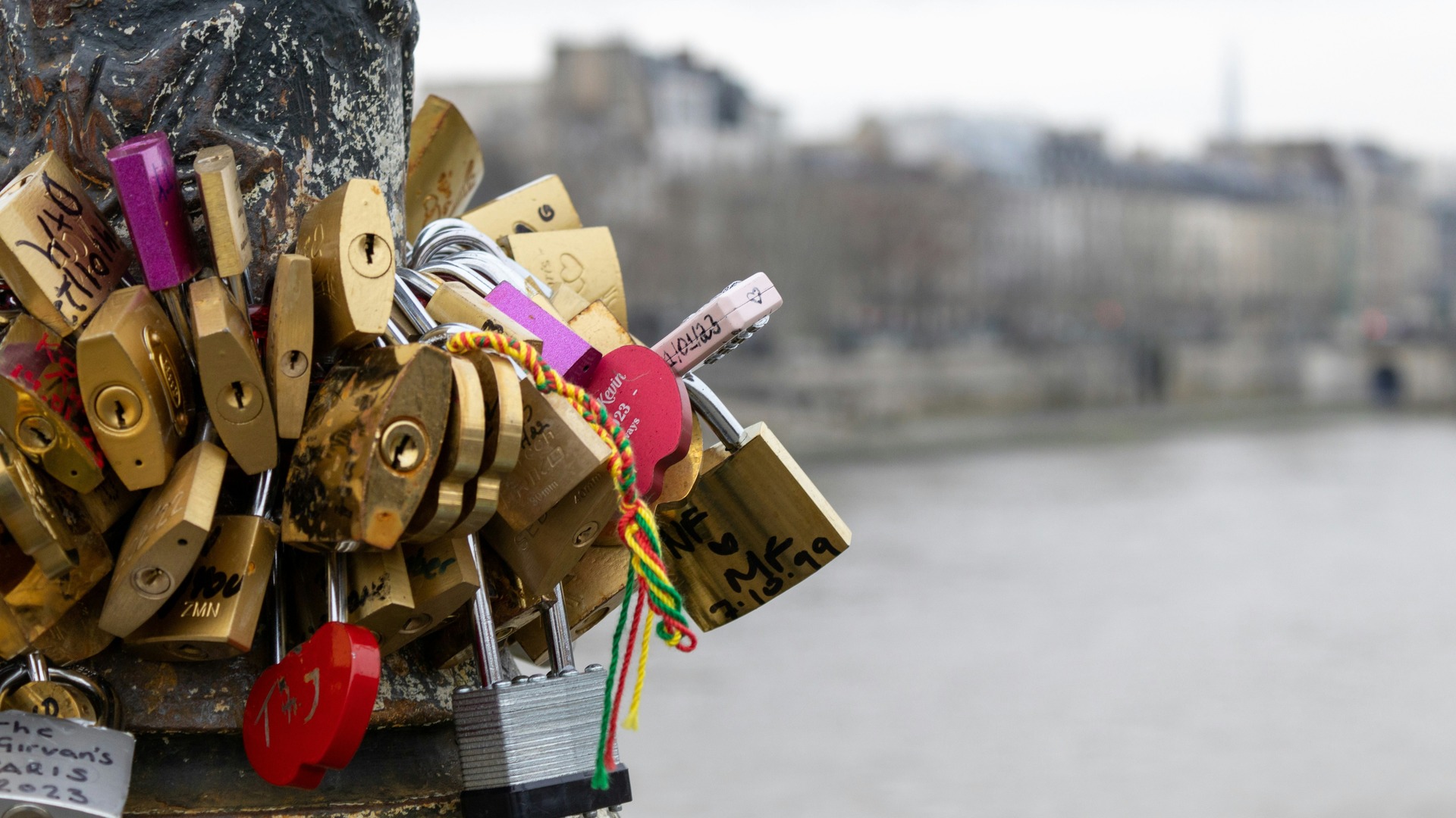 Candados de amor colgados en un poste junto al río Sena con París de fondo.
