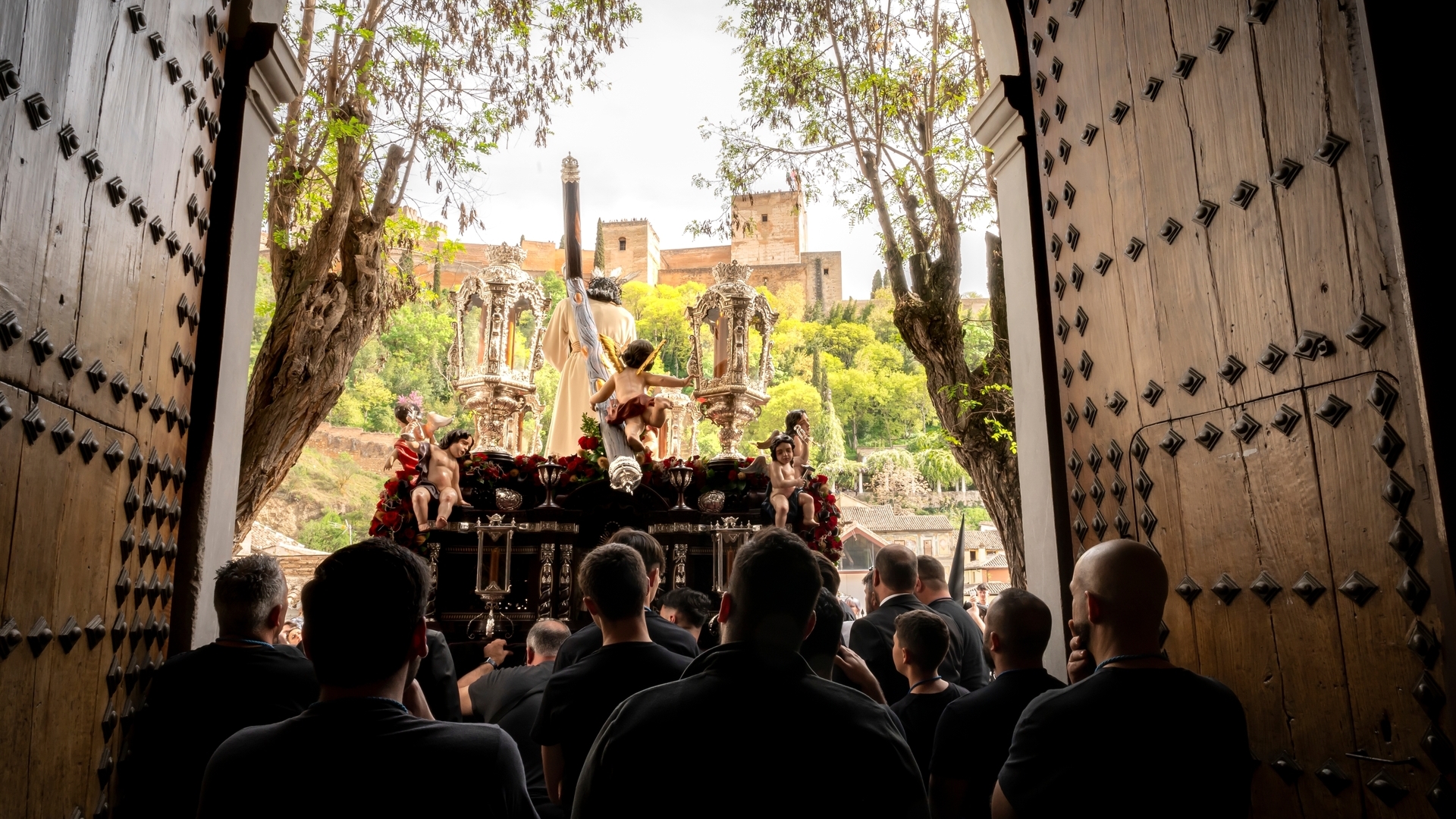 Paso de Semana Santa saliendo de iglesia con la Alhambra de Granada al fondo.
