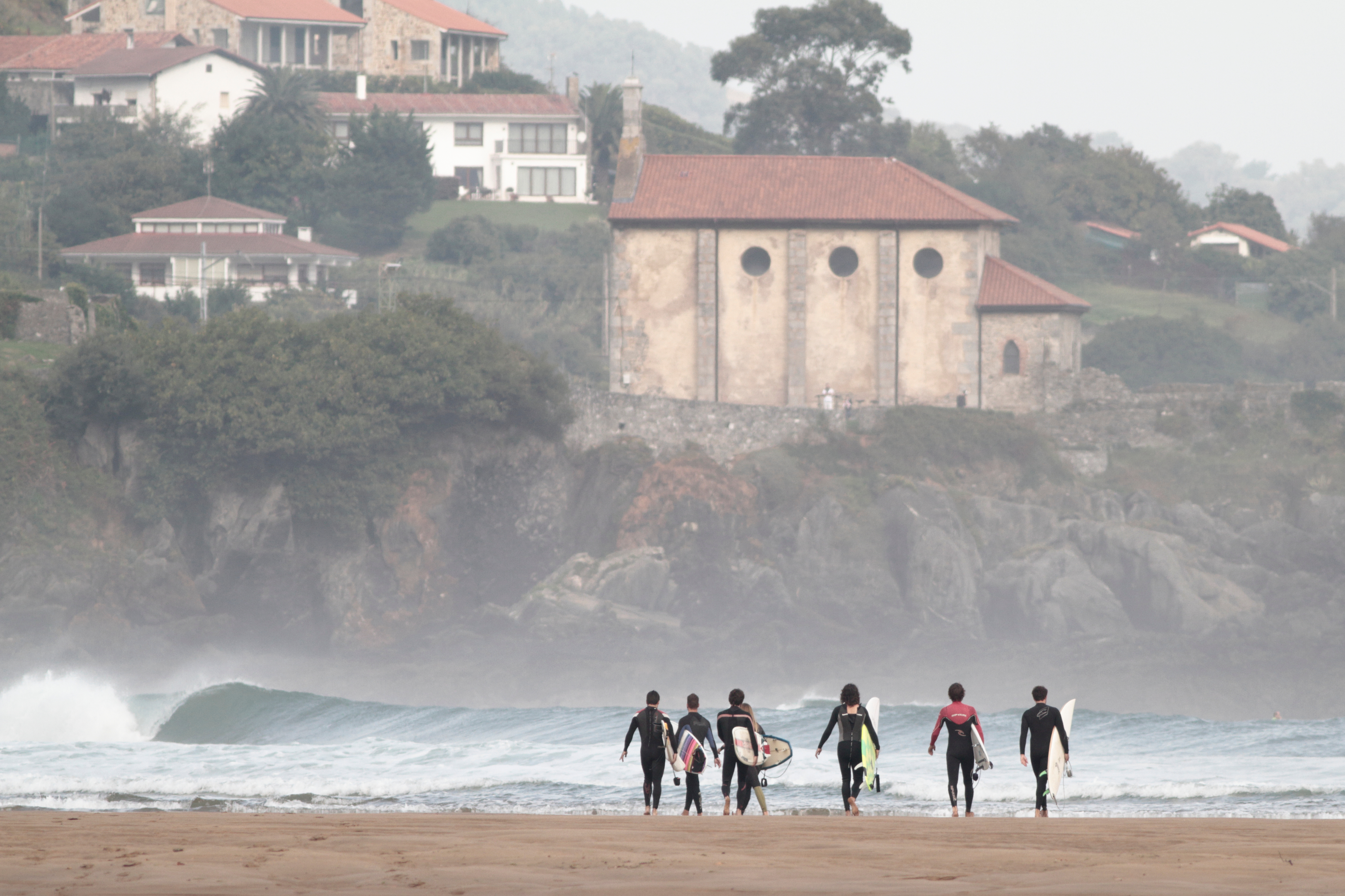 Surfistas playa mundaka y ermita de fondo
