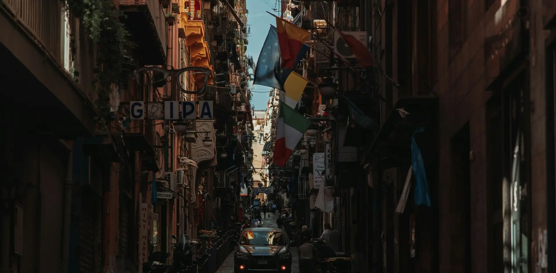 Calle estrecha y oscura de los Quartieri Spagnoli (Barrios Españoles) en Nápoles, Italia, con banderas colgantes.