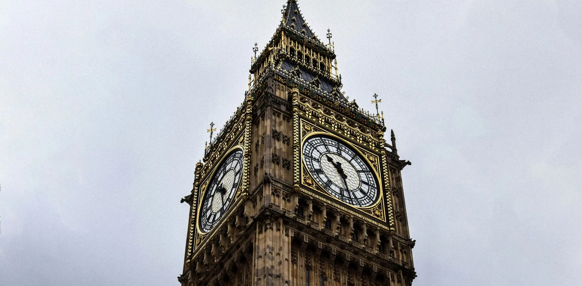 Primer plano de la Elizabeth Tower (Big Ben) en Londres, Inglaterra, con su reloj y detalles dorados bajo cielo nublado.
