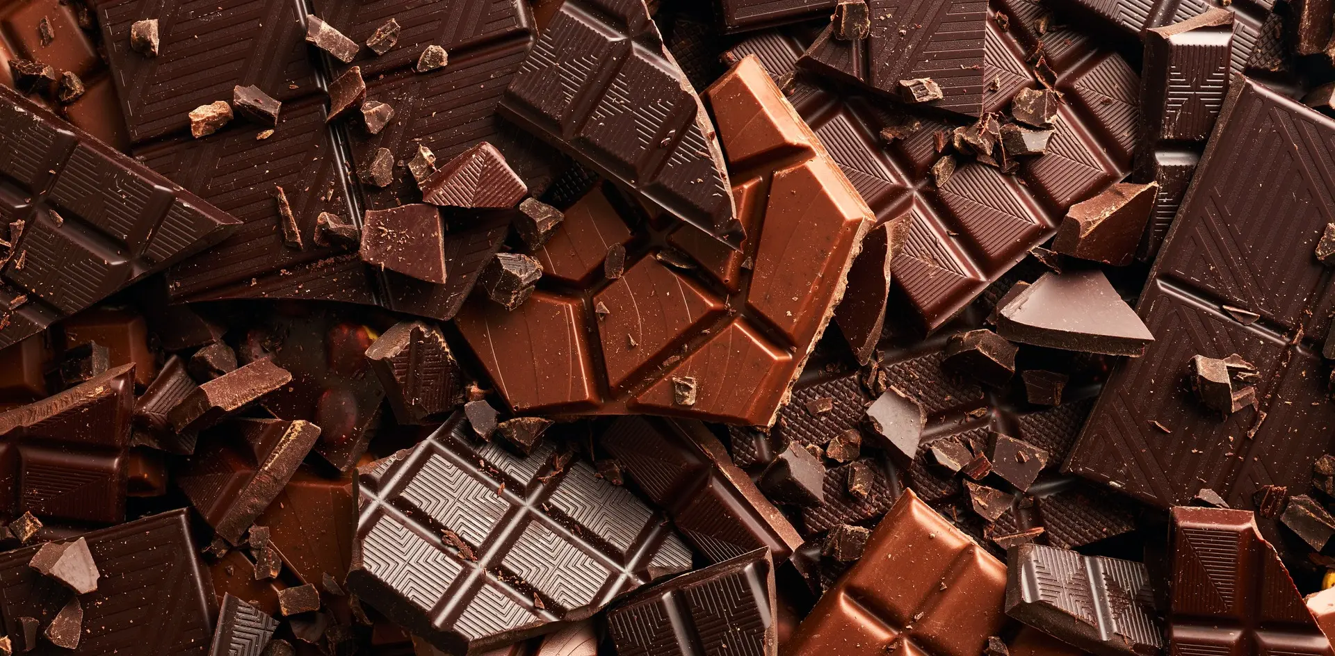 Primer plano de tabletas y trozos de chocolate negro y con leche, de Astorga o artesanal, apilados en textura densa.