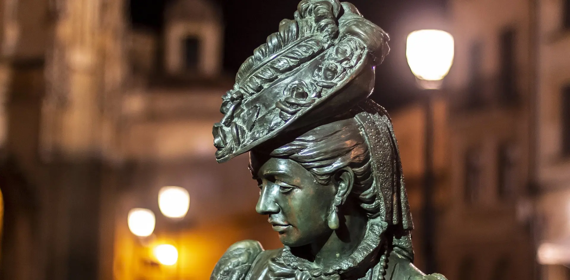 Estatua de bronce de 'La Regenta' (Ana Ozores) en Oviedo, iluminada por farolas urbanas en la oscuridad de la noche.