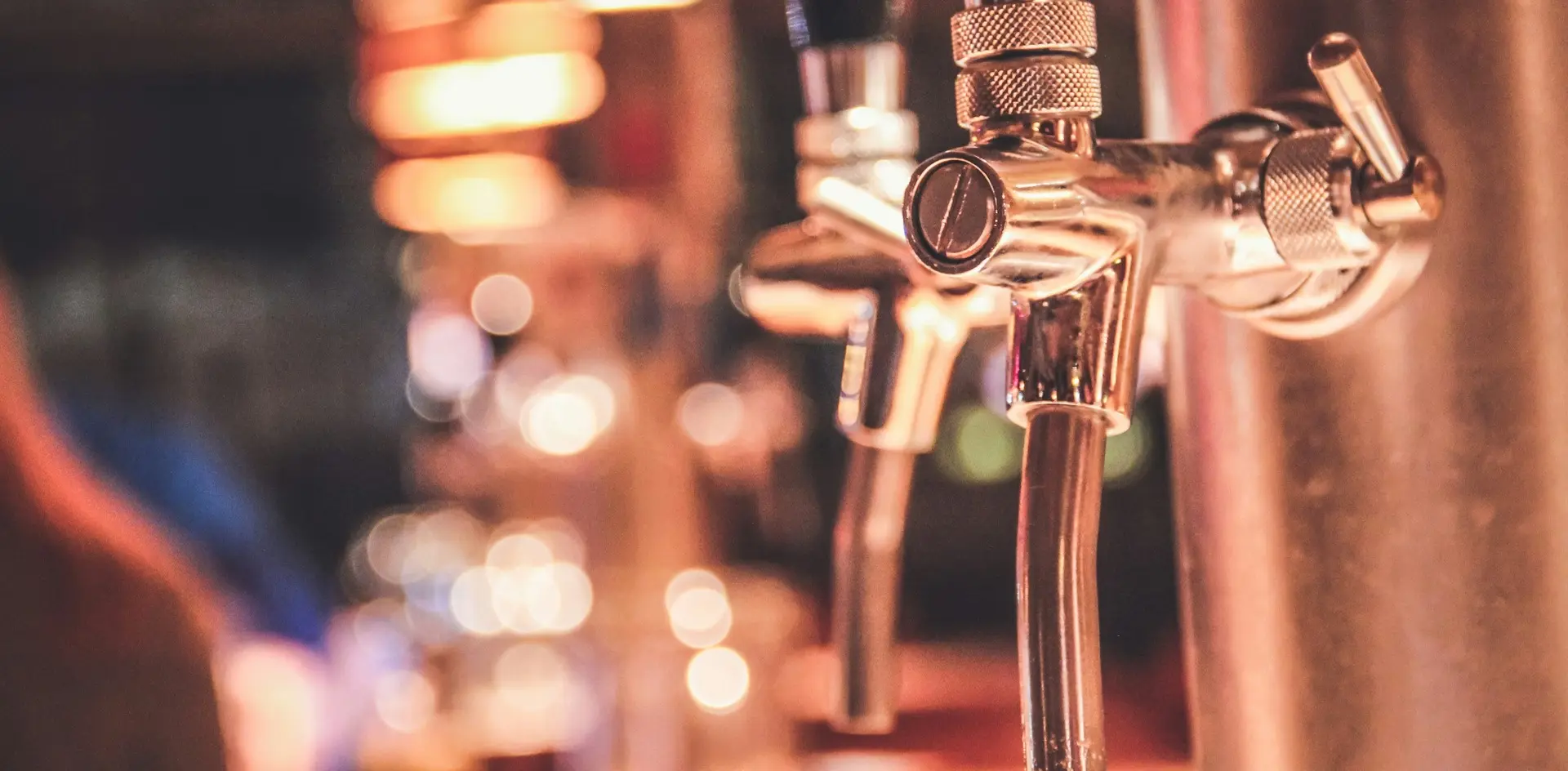 Grifos de cerveza metálicos en primer plano con bar de Berlín desenfocado.