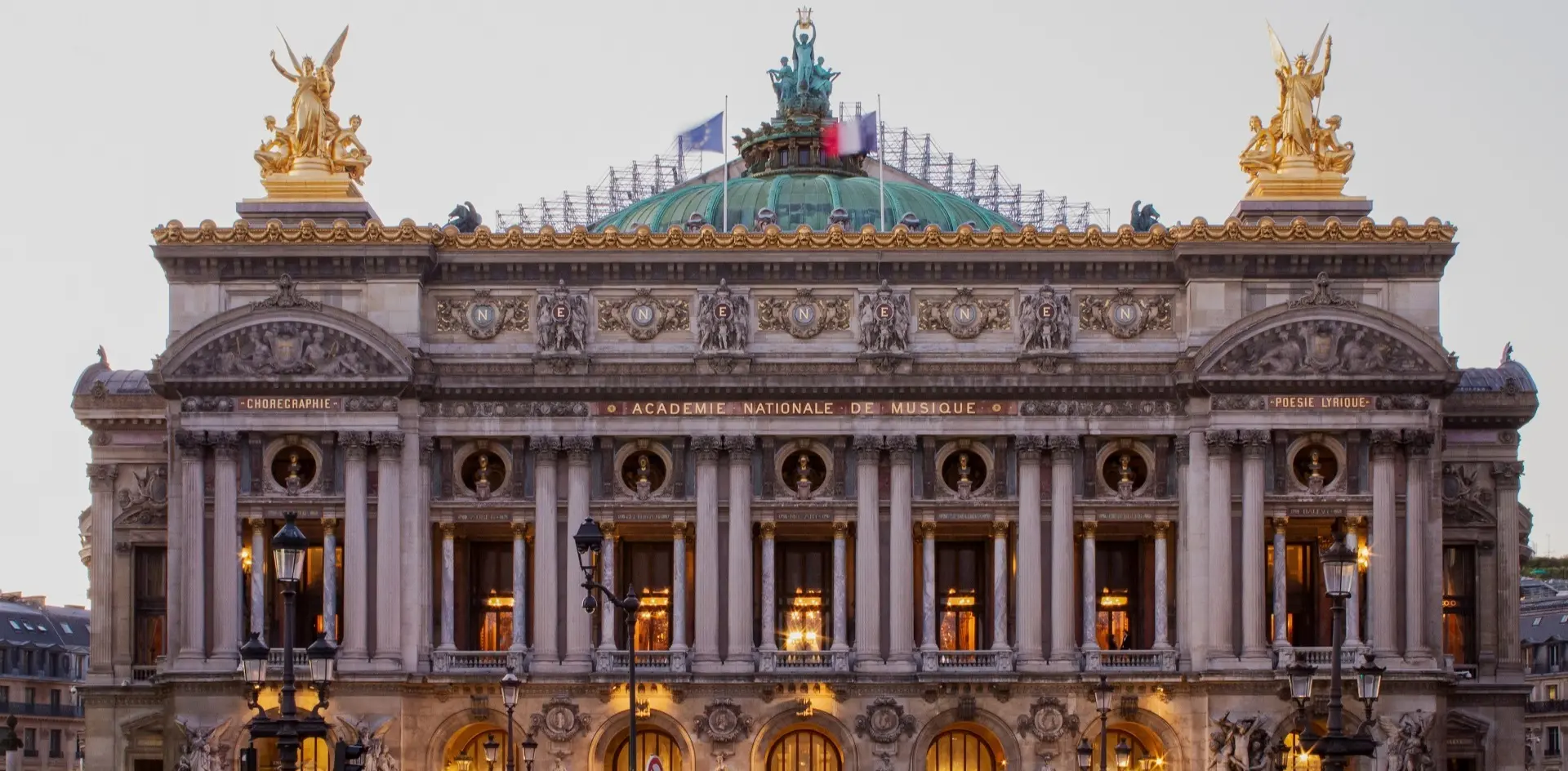 Fachada iluminada de la Ópera Garnier bajo el cielo del atardecer en París.