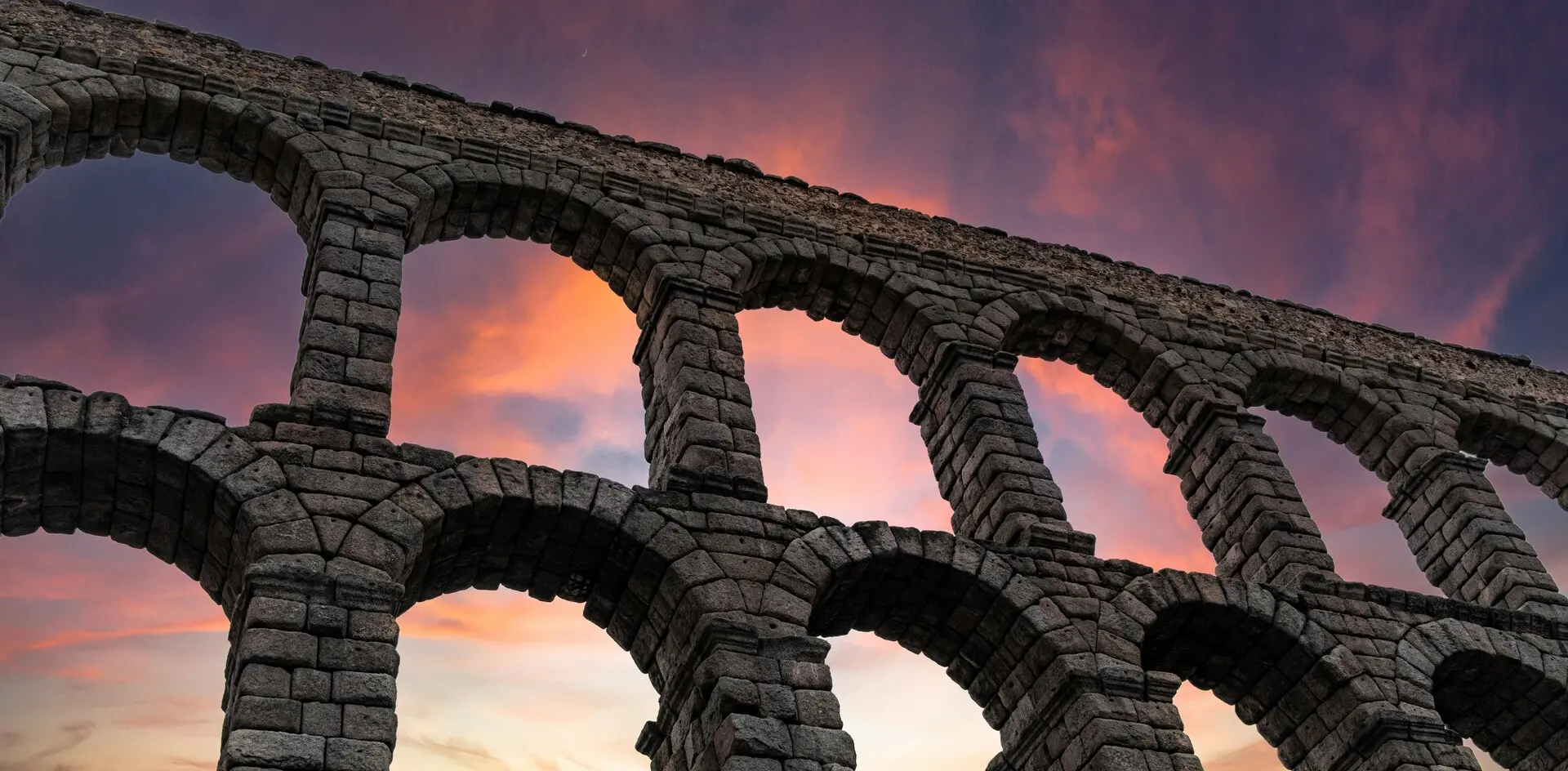 Arcos de piedra del Acueducto de Segovia bajo un cielo de atardecer rosado