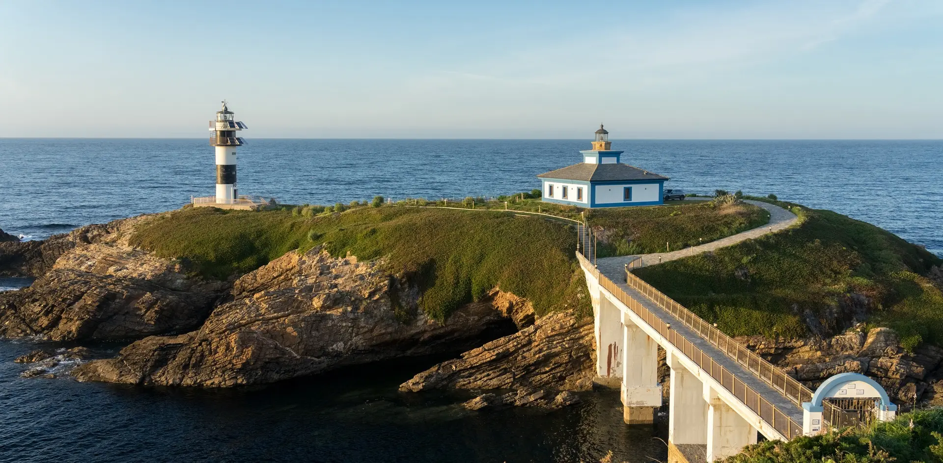 Faro de la Isla Pancha en Lugo, conectado por un puente a la costa. Edificio y torre blanca y negra junto al mar.