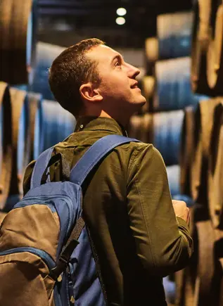 Visitante recorriendo una bodega tradicional entre barricas de vino en Oporto.