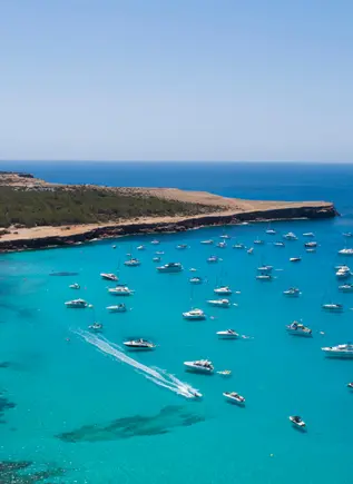Cala Saona vista desde lo alto, con barcos, vegetación y aguas de un azul intenso.