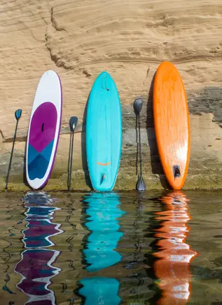 3 coloridas tablas de paddle surf apoyada en una roca de Mallorca