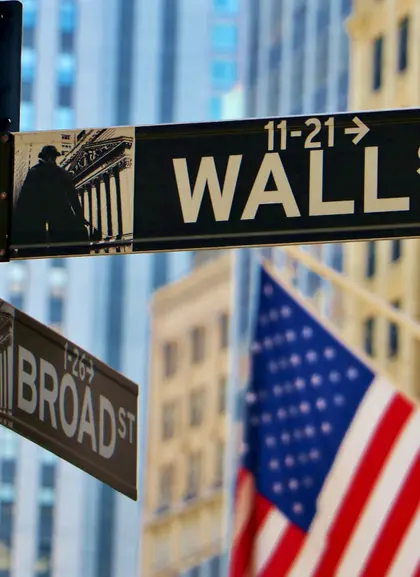 Señal de Wall Street y Broad Street con banderas estadounidenses y edificios del distrito financiero de Nueva York.
