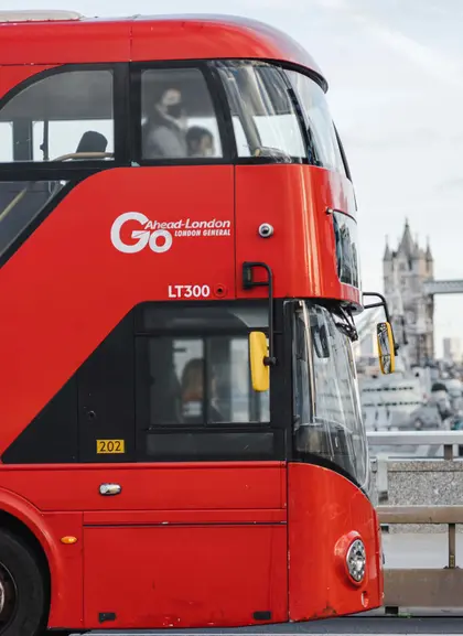 Autobús rojo de dos pisos cruzando Londres con el Puente de la Torre al fondo, típico del transporte londinense.