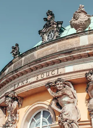 Detalle de la fachada del Palacio de Sanssouci en Potsdam, con estatuas de atlantes, inscripciones y la cúpula verde.