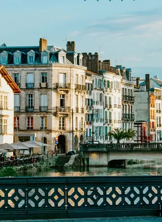Río y casas al atardecer en Bayona, con parejas apoyadas en el puente.