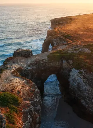 Vista aérea de la Playa de las Catedrales al atardecer, con sus arcos de roca bañados por el mar Cantábrico.