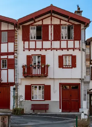 Fachadas típicas de casas vascas con madera roja y balcones floridos en el centro histórico de Espelette.