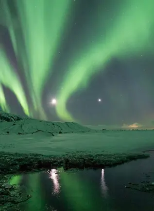Aurora boreal sobre un paisaje nevado en Islandia, con reflejos verdes iluminando el cielo y las montañas.