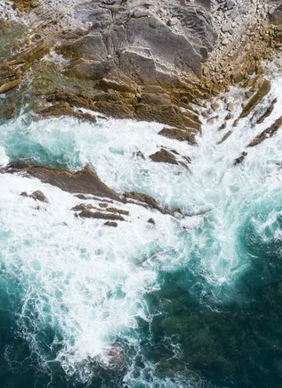 Vista aérea de las olas turquesas rompiendo contra las rocas y el acantilado en la costa de San Juan de Luz.