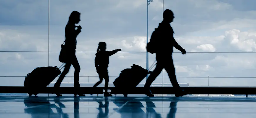 Familia en un aeropuerto, con maletas y equipaje, en una zona amplia con señalización y ventanales al fondo.