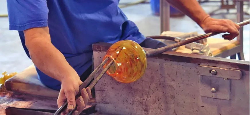 Maestro vidriero trabajando con vidrio fundido utilizando la técnica tradicional de soplado. 