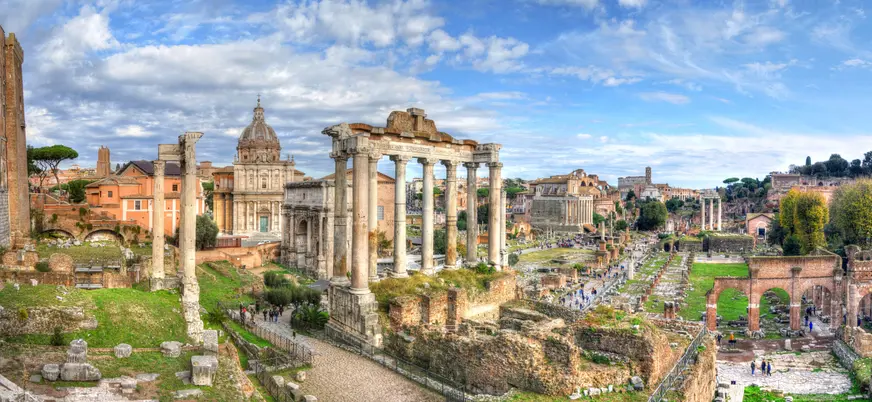 Columnas del Templo de Saturno en el Foro Romano con cúpula de iglesia al fondo.